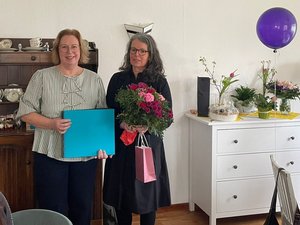 Zwei Frauen bei einer Verabschiedung: Sabine Brüning (rechts) hält Blumen und ein Geschenk, Geschäftsführerin Martina Fisser (links) ein Erinnerungsalbum. Im Hintergrund sind weitere Geschenke und ein Luftballon zu sehen.